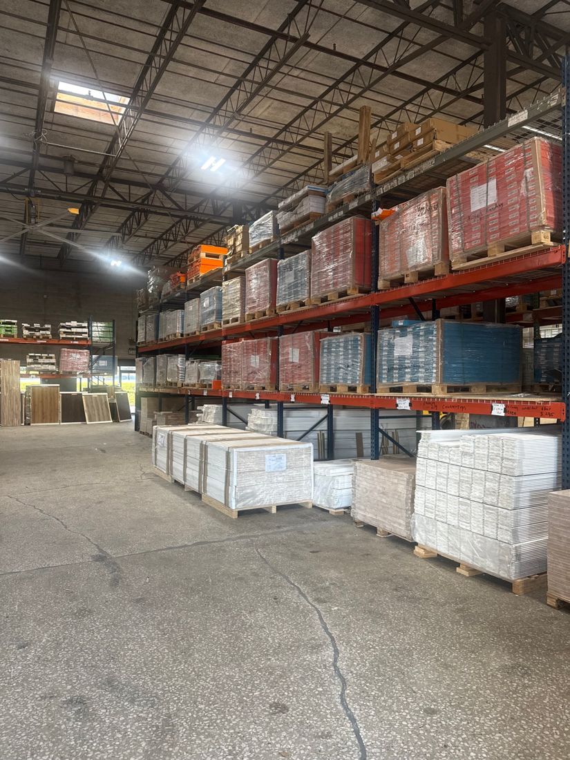 Tall racks of flooring pallets and primed trim along a warehouse aisle